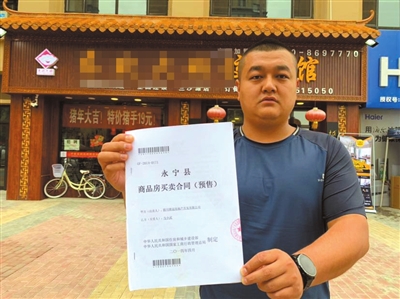 馬先生在自己的營業(yè)房前向記者出示他的購房合同。